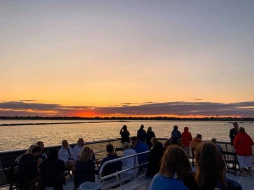 People enjoying a sunset cruise, with a vibrant sunset reflecting on the water in the background.
