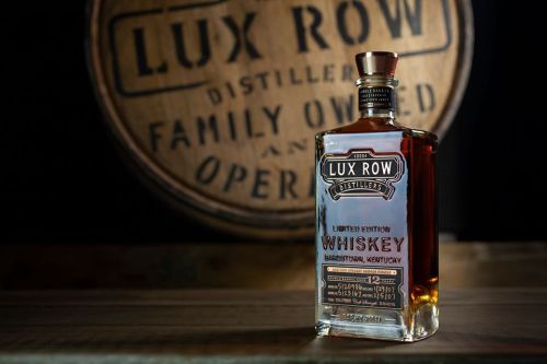 A bottle of Lux Row Limited Edition Whiskey in front of a wooden distillery sign.
