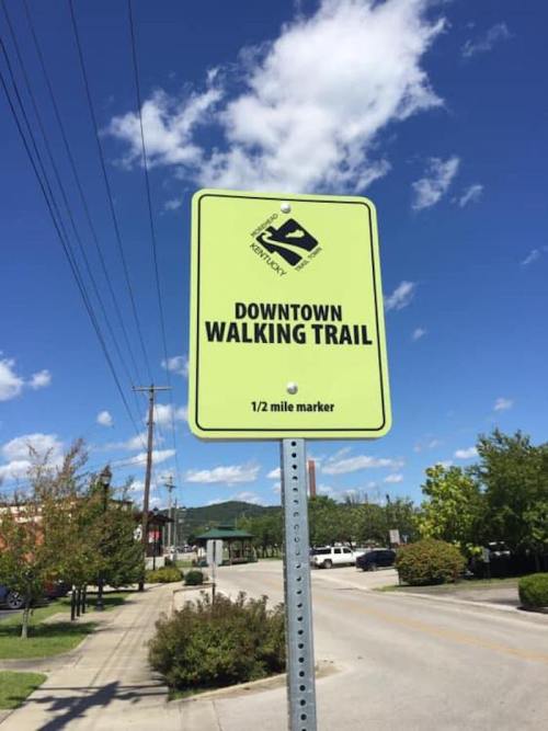 Bright green sign indicating a 1/2 mile marker for the downtown walking trail, with a clear blue sky in the background.