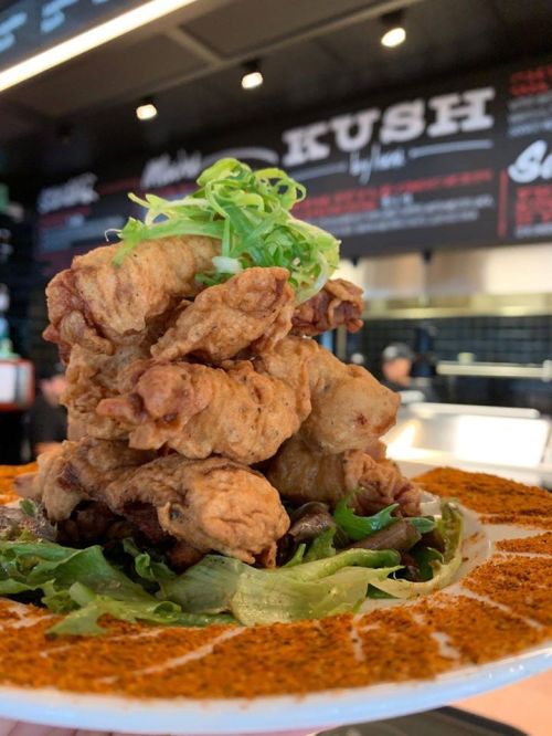 A plate of crispy fried chicken piled high, garnished with green onions, served on a bed of greens with a spicy seasoning.