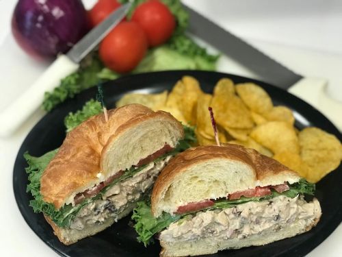 A croissant sandwich filled with chicken salad, lettuce, and tomato, served with potato chips on a black plate.