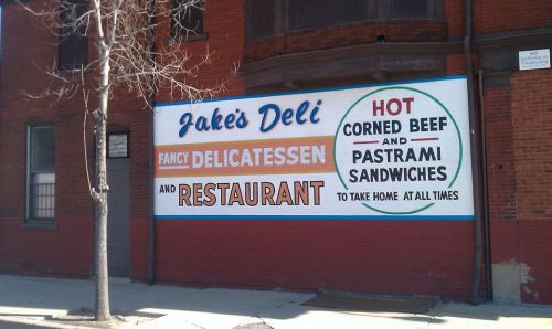 Sign for Jake's Deli, featuring "Hot Corned Beef and Pastrami Sandwiches" and highlighting its delicatessen and restaurant.