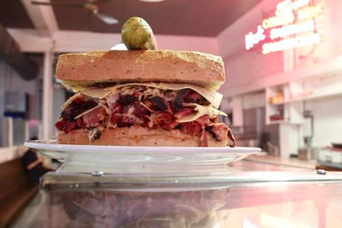 A towering sandwich filled with layers of meat, cheese, and topped with a pickle, served on a plate.