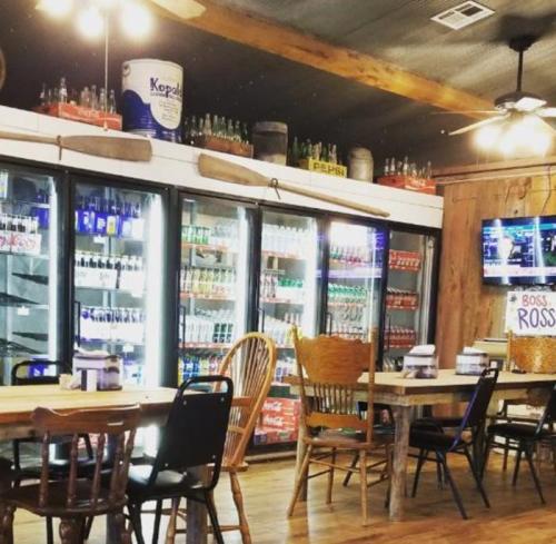 A rustic diner interior with wooden tables, chairs, and a drink cooler filled with various beverages.