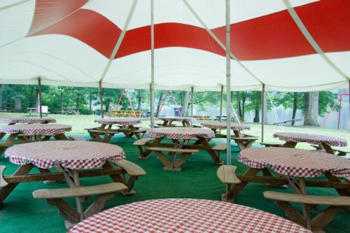 A large tent with red and white stripes, featuring several picnic tables covered in checkered tablecloths.