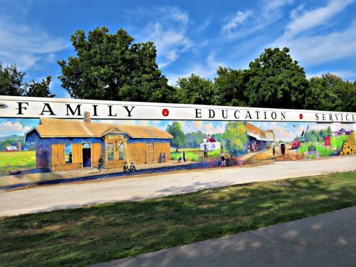 A colorful mural depicting a rural scene with buildings, trees, and people, alongside the words "Family Education Services."