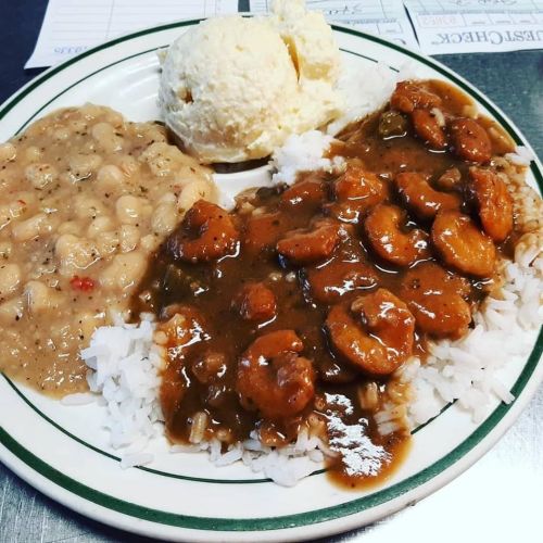 A plate of rice topped with shrimp stew, beans, and a scoop of ice cream on the side.