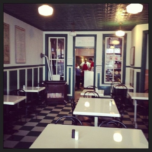 A vintage diner interior with empty tables, green and white decor, and staff visible in the kitchen area.