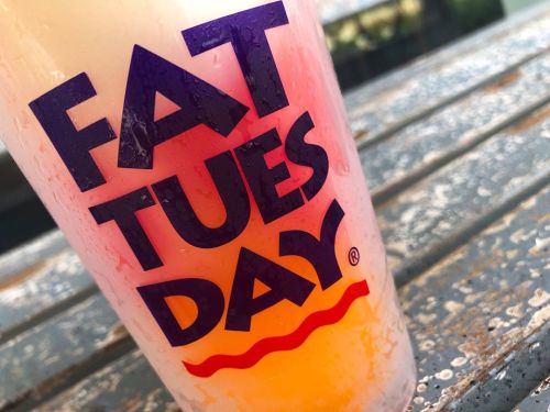 A colorful drink in a cup with the text "FAT TUESDAY" on a weathered surface.