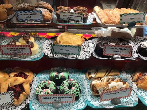 A display case filled with various baked goods, including cakes, pastries, and cookies, labeled with their names.