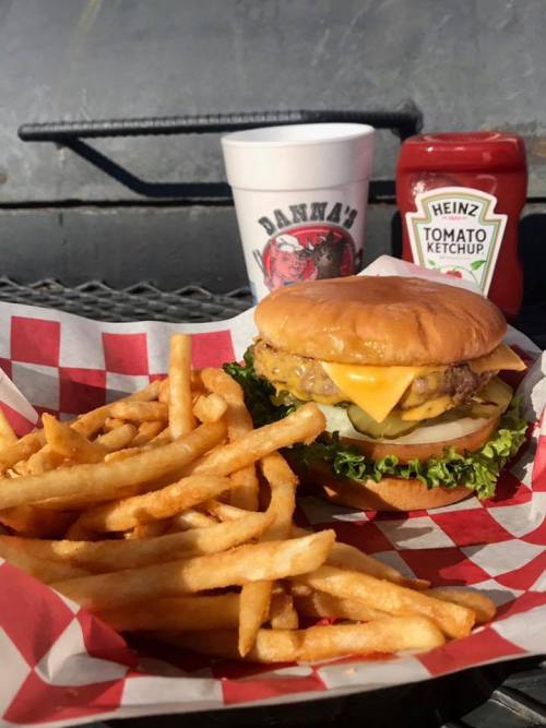 A delicious cheeseburger with lettuce and pickles, served with crispy fries, ketchup, and a drink in the background.