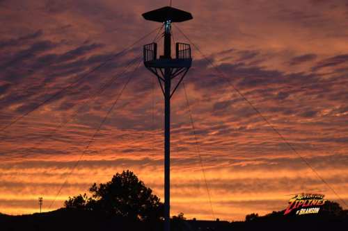 A silhouette of a zipline tower against a vibrant sunset with colorful clouds.