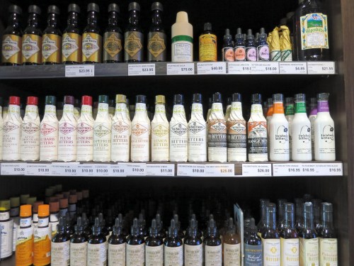 A shelf displaying various bottles of bitters and flavoring extracts in different sizes and colors.