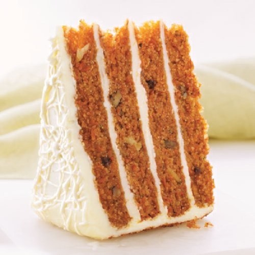 A slice of layered carrot cake with cream cheese frosting and visible nuts, set against a light background.