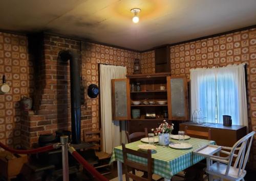 A cozy vintage kitchen with a wooden table, patterned wallpaper, a stove, and a cupboard filled with dishes.