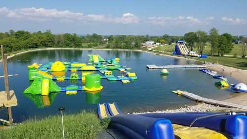 A colorful inflatable water park on a lake, featuring slides, obstacles, and a sandy beach area.