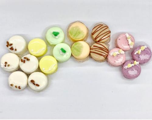 A colorful assortment of macarons in various flavors, arranged in a rainbow pattern on a white background.