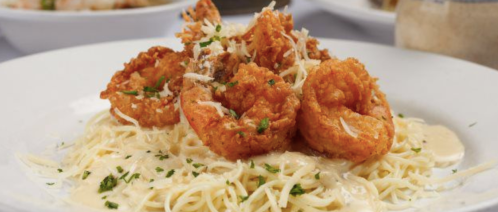 A plate of pasta topped with crispy shrimp and sprinkled with cheese and herbs.