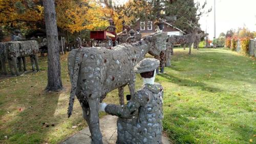 A stone sculpture of a person milking a cow, surrounded by other similar sculptures in a colorful outdoor setting.