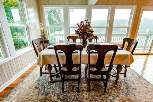 A cozy dining area with a table set for four, surrounded by large windows and a floral centerpiece.