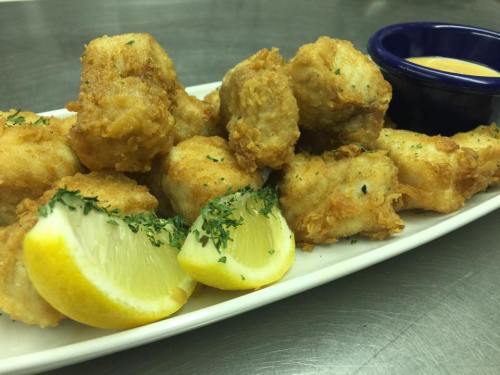 A plate of golden-brown fried bites garnished with parsley and lemon wedges, served with a small bowl of dipping sauce.
