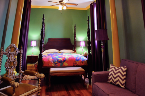 A vibrant bedroom with a four-poster bed, colorful bedding, purple curtains, and stylish furniture.