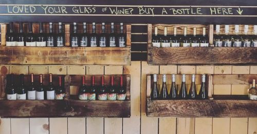Shelves displaying various bottles of wine with a chalkboard sign inviting customers to buy a bottle.