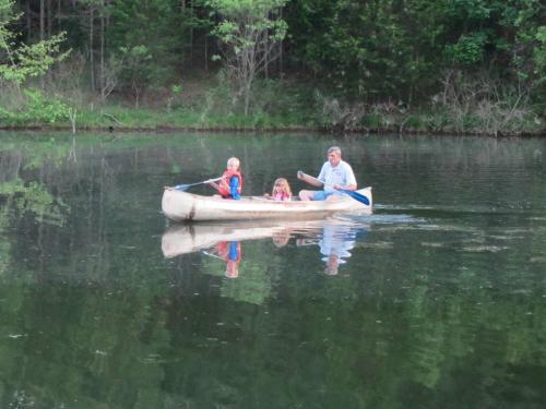 A man and two children paddle a canoe on a calm lake surrounded by trees.