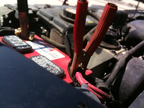 Close-up of a car battery with red jumper cables connected to the terminals.
