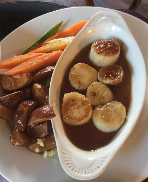 A plate featuring seared scallops in sauce, roasted potatoes, and colorful carrots.
