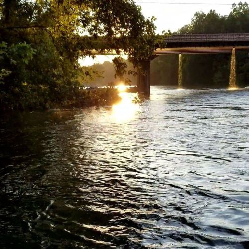A serene river scene at sunset, with sunlight reflecting on the water and a bridge in the background.