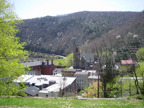 A scenic view of a small town nestled in green hills, featuring buildings and a church against a backdrop of trees.