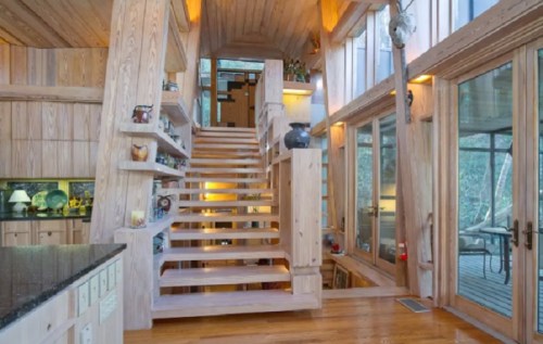 A modern wooden staircase leads to a bright, open space with large windows and natural light.