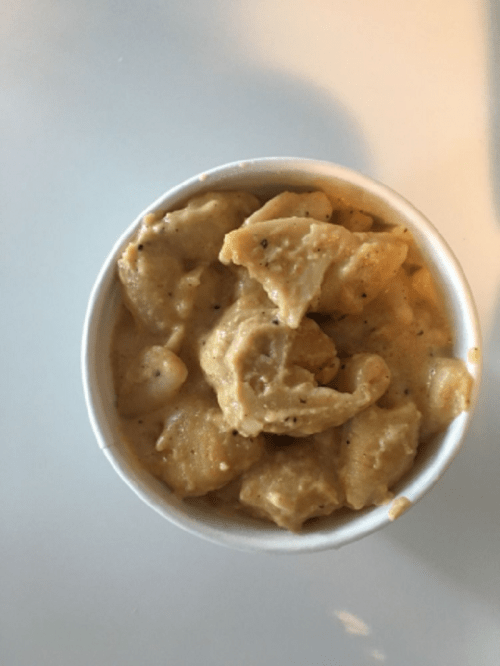 A cup of creamy, seasoned dumplings in a light sauce, served on a white surface.
