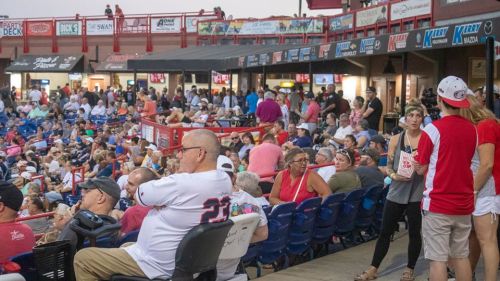A crowded stadium with fans watching a game, seated in bleachers and standing in various areas, enjoying the event.