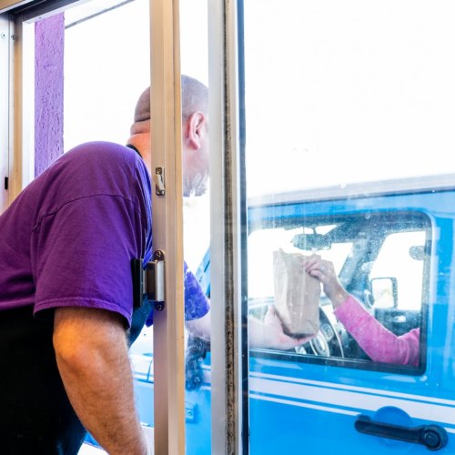 A worker hands a bag of food to a customer through a drive-thru window.