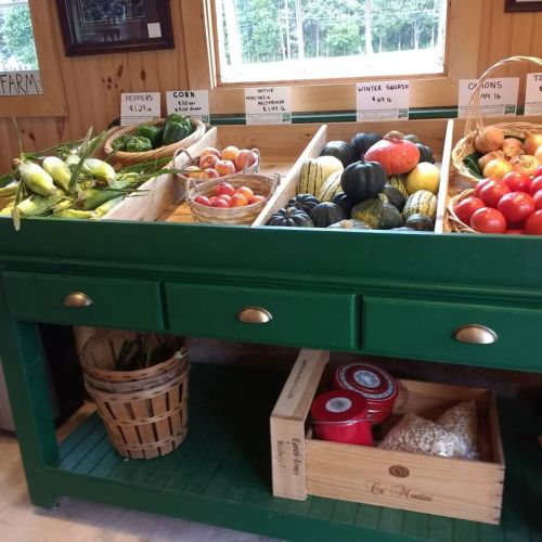 A green display table filled with fresh vegetables and fruits, including peppers, corn, squash, and tomatoes.