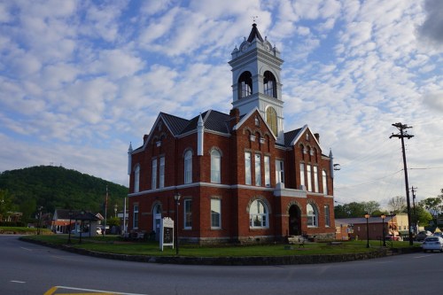 Historic brick building with a clock tower, surrounded by a grassy area and a cloudy sky in the background.