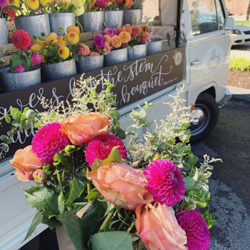 A flower truck displays vibrant bouquets of pink and orange flowers, with potted blooms in the background.