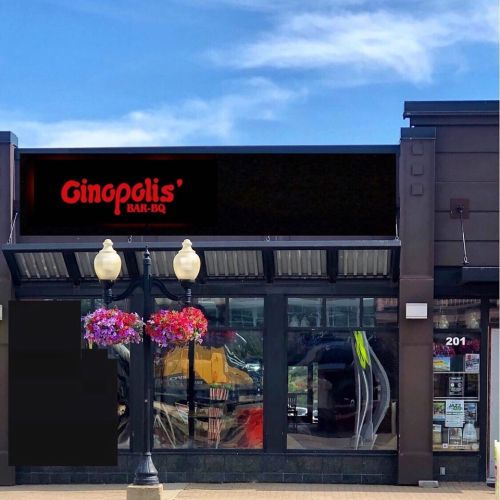 Exterior of Ginopolis' Bar-B-Q restaurant with colorful flower baskets and a clear blue sky.