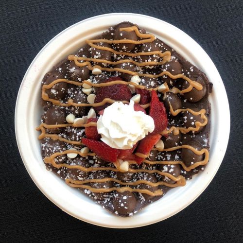 A dessert bowl featuring chocolate sauce, strawberries, whipped cream, and drizzled peanut butter.