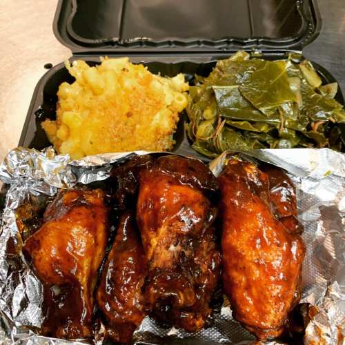 A takeout container with BBQ chicken, macaroni and cheese, and collard greens.