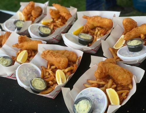 A close-up of several baskets of fried fish and chips, served with lemon wedges and dipping sauce.