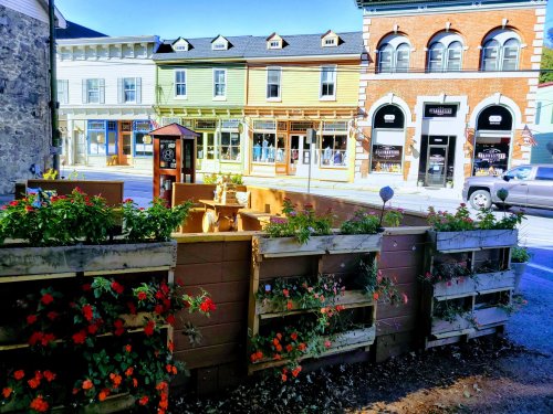 A quaint street scene featuring colorful buildings and a flower-filled wooden planter in the foreground.