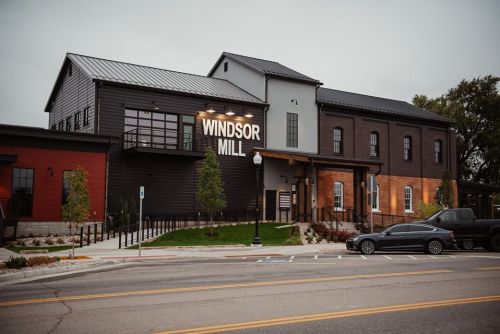 Exterior view of Windsor Mill, a modern building with a mix of brick and metal, surrounded by greenery and parked cars.