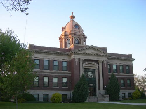 Historic brick building with a prominent dome, surrounded by trees and a well-maintained lawn under a clear sky.