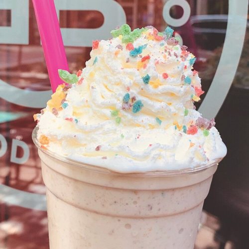 A creamy milkshake topped with whipped cream and colorful sprinkles, served with a pink straw.