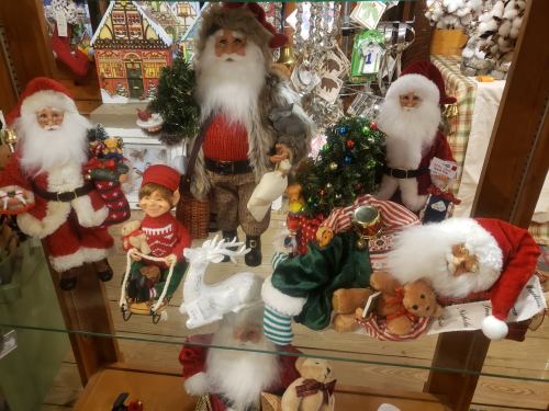 A display of festive holiday figurines, including Santa Claus, elves, and reindeer, surrounded by Christmas decorations.