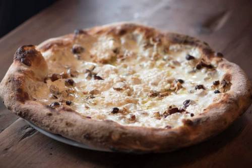 A freshly baked pizza with a golden crust, topped with cheese and small pieces of meat, on a wooden table.