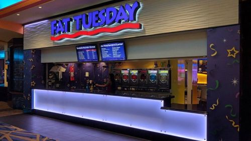 A brightly lit Fat Tuesday bar with a menu board and colorful drink machines in a festive setting.